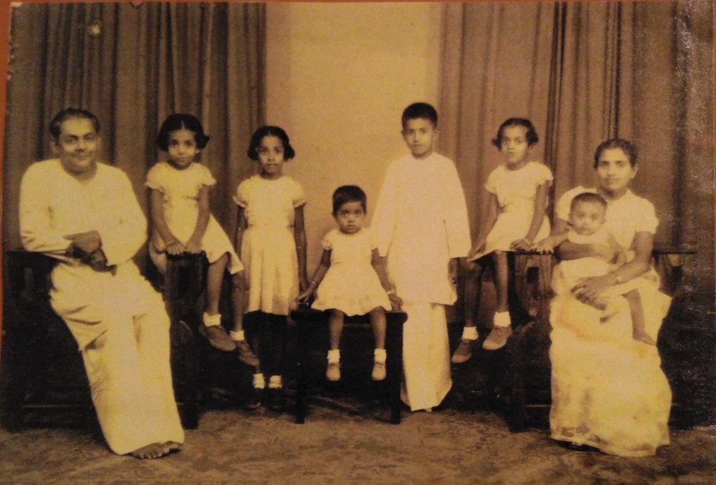 family photo vintage colour formal portrait six people man on left on chair small girls and tall boy another girl and small baby in woman's arms