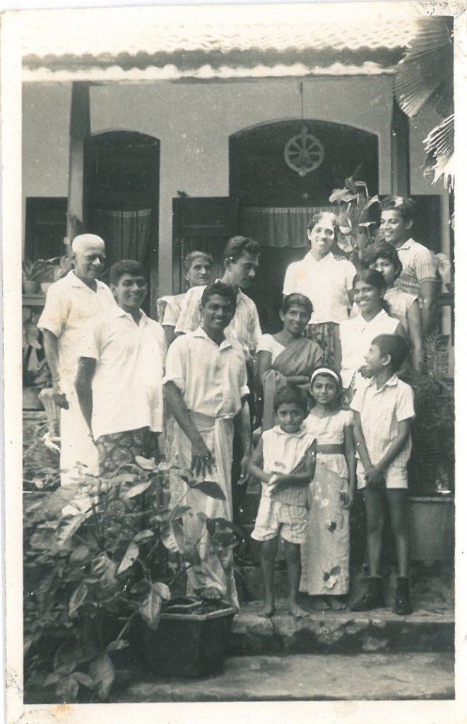 family photo black and white in front of house small kids in front and men and women behind all smiling