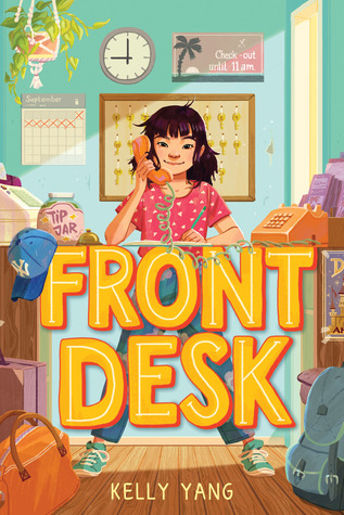 Front desk in large orange and yellow letters standing behind them young girl with dark hair and red spotted tshirt and jeans on red phone clock and keys behind plant and calendar to her right blue cap and tip jar on right phone base on left bags on floor in front of girl