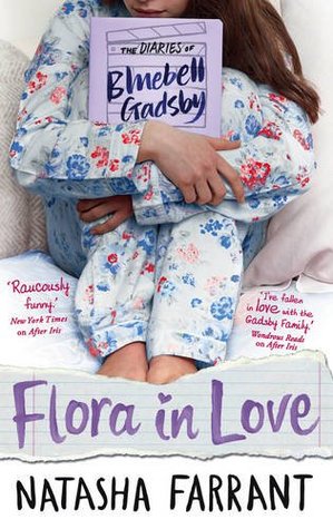 young girl in blue and red flowery pyjamas holding book under arms sitting on bed. text at bottom Flora in love in purple. Natasha Farrant in black.
