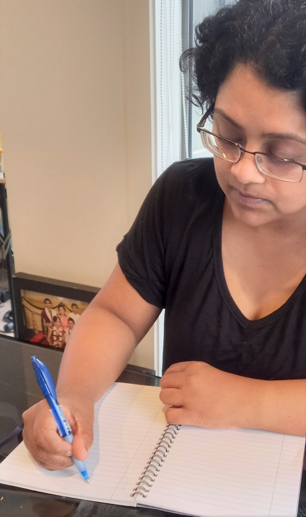 woman in black top with glasses writing on book with blue pen front profile