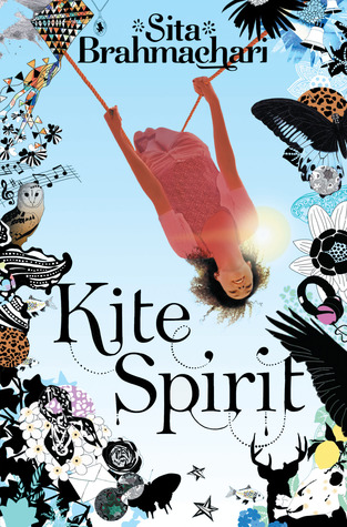 blue cover background of sky and sun shining from above shoulder of image of young girl taken from mid-flight on swing while upside down. around edges images of flowers, woodland creatures, bells, kites, musical notes. large black letters at middle bottom read Kite Spirit. smaller letters at top read Sita Brahmachari.