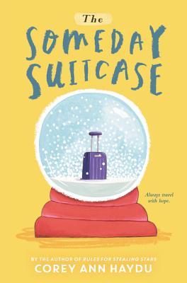 cover image in yellow background. large snowglobe in middle with red base. inside snowglobe is suitcase. blue letters across top reads The Someday Suitcase. white letters along bottom reads Corey Ann Haydu.