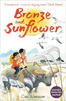 cover image of two small children riding on top of buffalo in fields. small buildings in middle ground. cranes flying in sky. orange yellow sun in middle. red letters over sun reads Bronze and Sunflower.