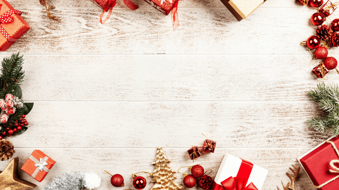 image of table with Christmas themed gifts, decorations, greenery around edges. red boxes, red baubles, green leaves and silver baubles.