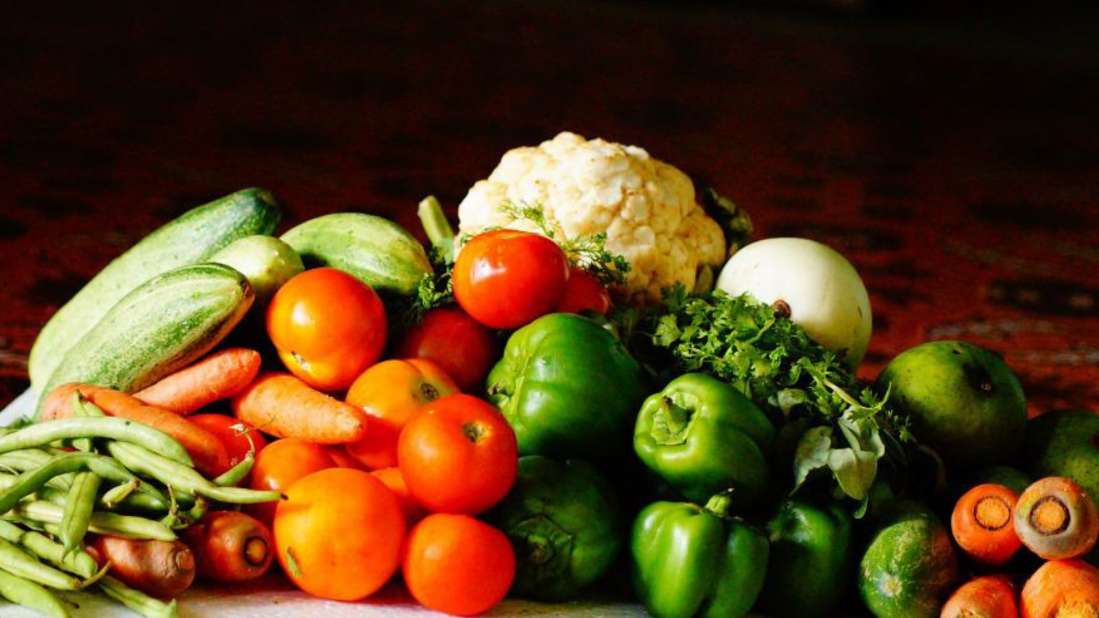 image of pile of fresh vegetables on table with dark background. from beans, carrots, tomatoes, green peppers to cauliflower and lemons.