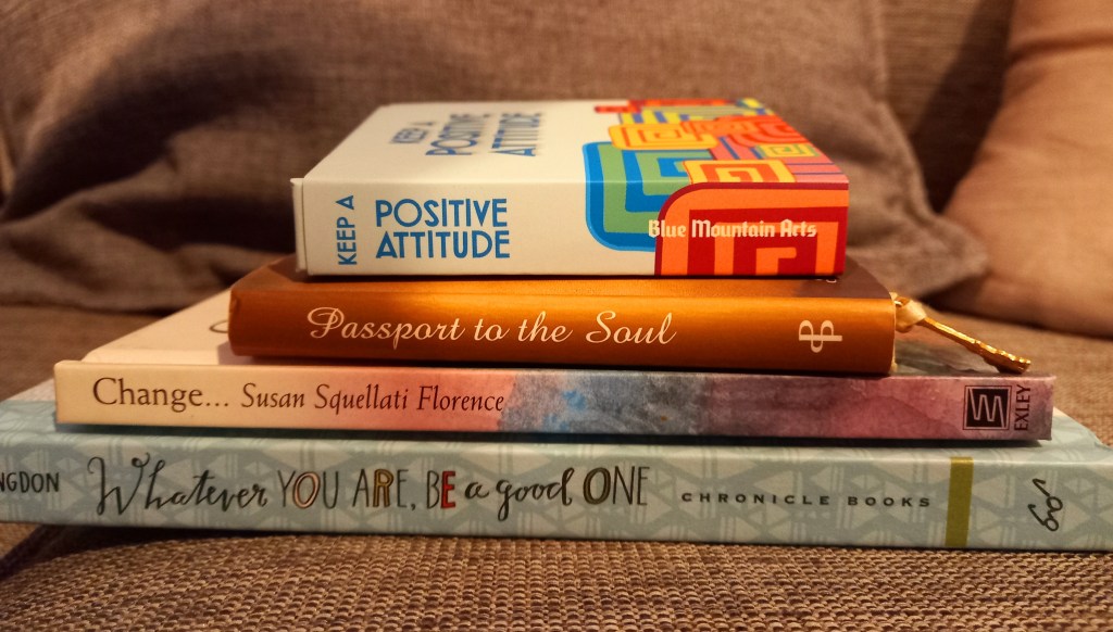 Image of small pile of books on grey surface. bright and colourful spines of four books. bottom larger than other three above.