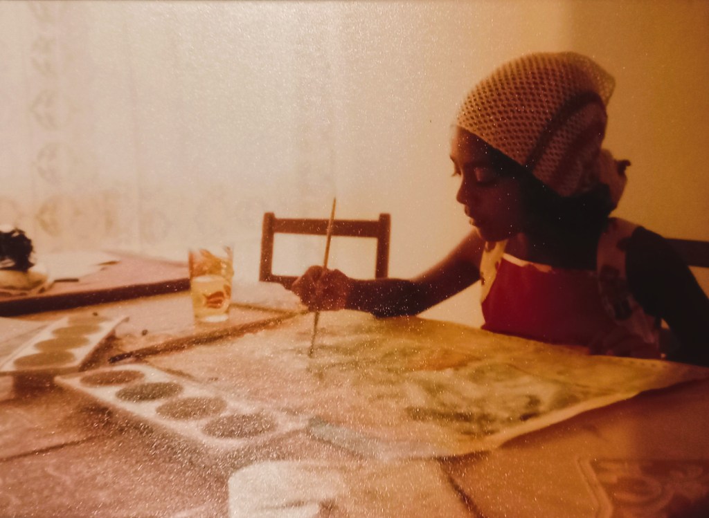 image of young girl in red dress and white head scarf painting on table. lace curtains in back.