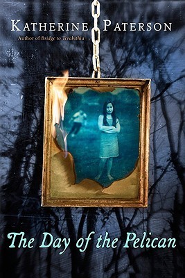 image of gold frame hanging on chain. photograph inside of young girl and boy in black and white. dark black trees in night in background. white letters on bottom reads The Day of the Pelican.