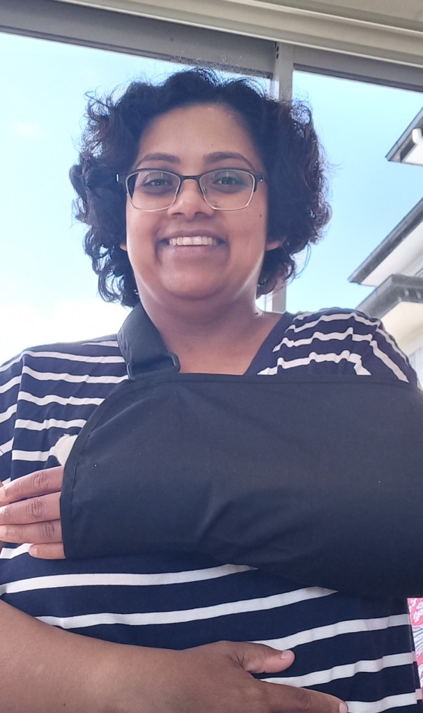 author with arm in black sling wearing white and blue stripes. blue sky behind.