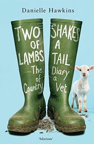 cover image of pair of green boots with small white lamb looking out from behind the right one. light blue background. dirt along edge of bottom and in middle between boots. white words painted on left boot reads Two of Lambs The of Country and right boot has Shakes A Tail Dairy a Vet. black letters above boots reads Danielle Hawkins.