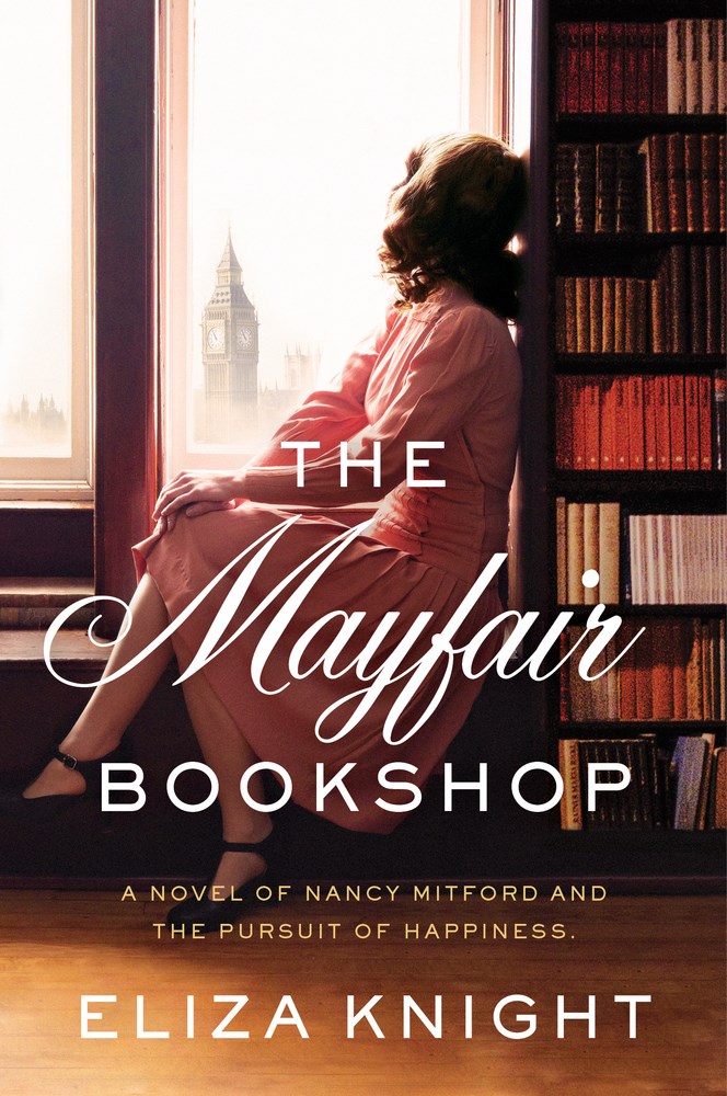 cover image has woman in pink dress and dark hair seated by window looking out at London landscape of Big Ben and Tower of London. bookshelf with books behind her on right. white letters across her reads The Mayfair Bookshop and below Eliza Knight. small yellow letters between these reads A Novel of Nancy Mitford and The Pursuit of Happiness.