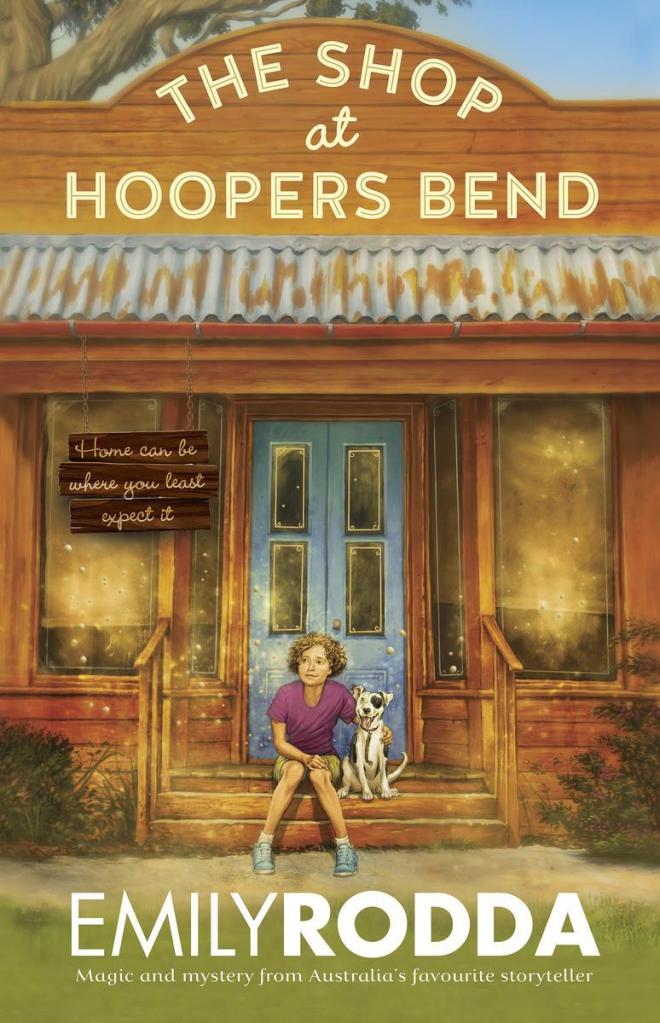 cover image of young girl in purple top and shorts sitting on steps to shope with white dog with black spot over one eye. blue door behind them and two large windows beside door. blue rusty awning above and curved storefront with large white letters around it reads The Shop at Hoopers Bend. little bit of blue sky and tree branch over brown building. green bushes beside steps and green ground has large white letters on it reading Emily Rodda.