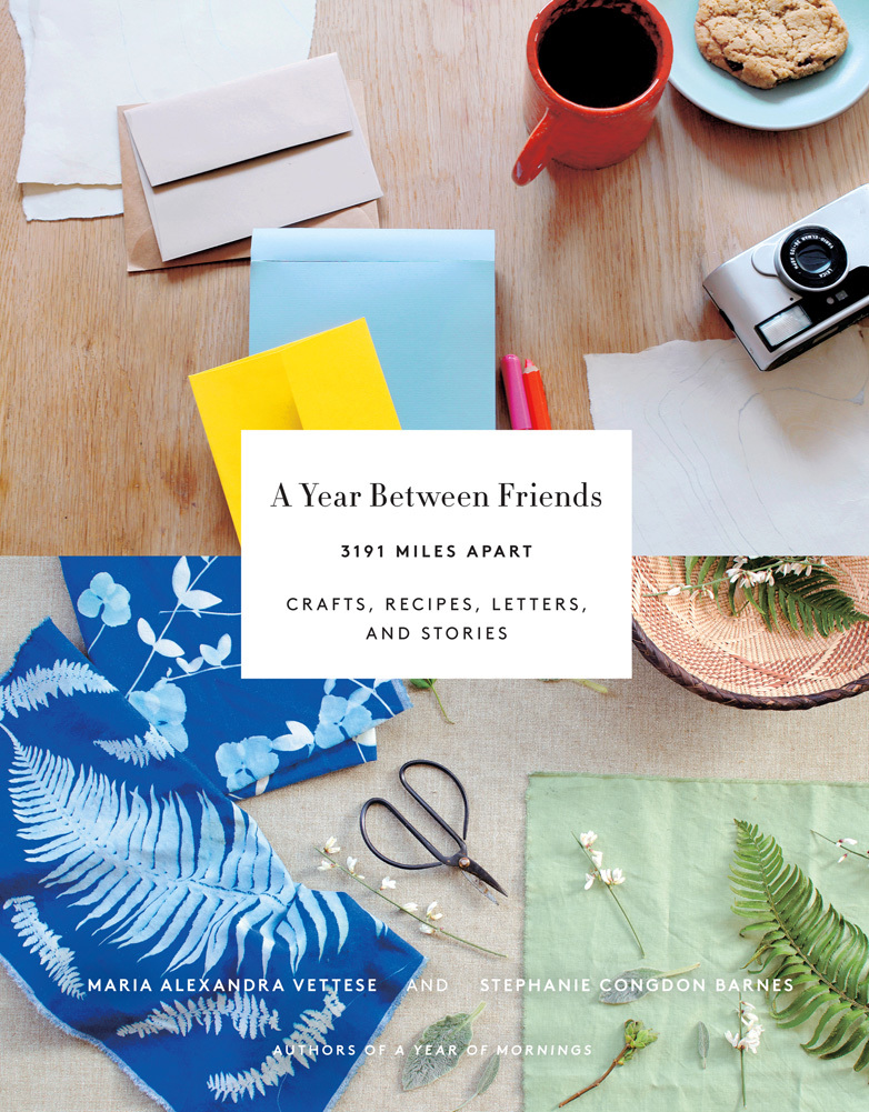cover image made up of two photographs. top one of table top with red coffee cup and blue plate and cookie at top right, small camera below and paper and different coloured envelopes on left with two red pens in middle. bottom photograph has green cloth with leaf and flowers on bottom right, small scissors in middle, blue floral material on left and edge of basket at top. between both in middle small white box with black typography that reads A Year Between Friends 3191 Miles Apart Craft, Recipes, Letters, And Stories. smaller white letters across bottom of photograph of material reads Maria Alexandra Vettese And Stephanie Congdon Barnes Authors of a Year of Morning.
